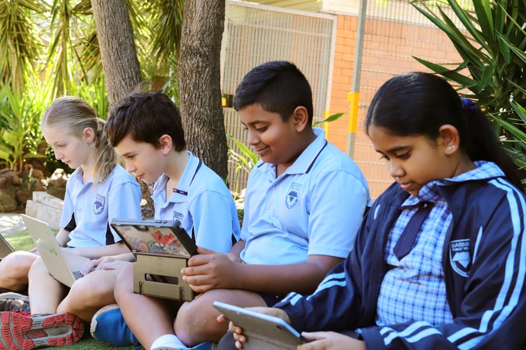 4 students sitting outside on devices