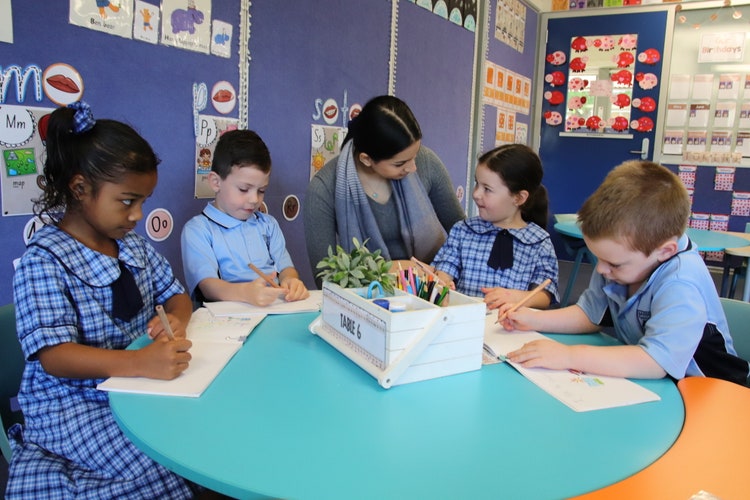 teacher sitting at a table in class talking to 4 students